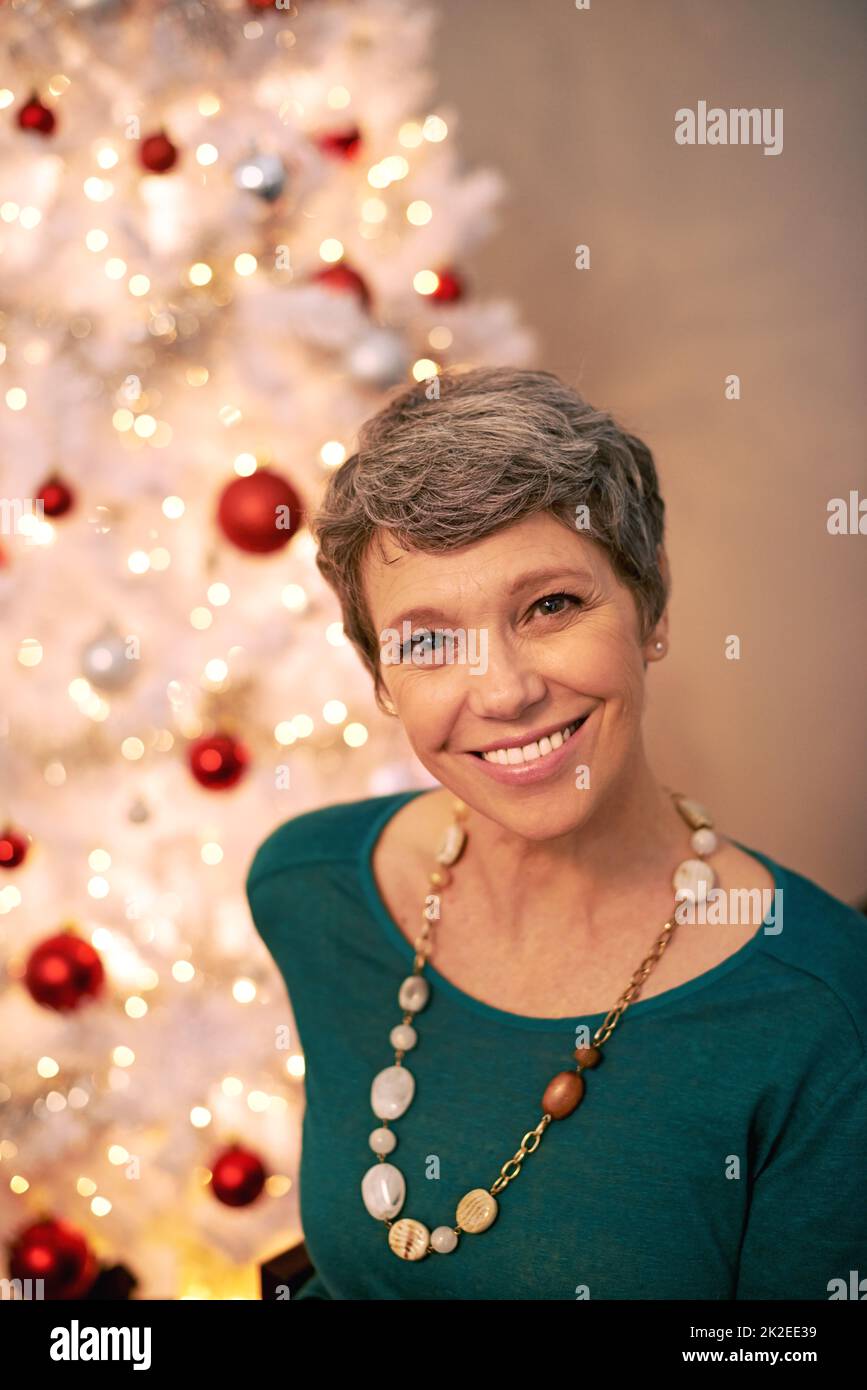 È il periodo più meraviglioso dell'anno. Ritratto corto di una donna matura felice seduta davanti al suo albero di Natale. Foto Stock
