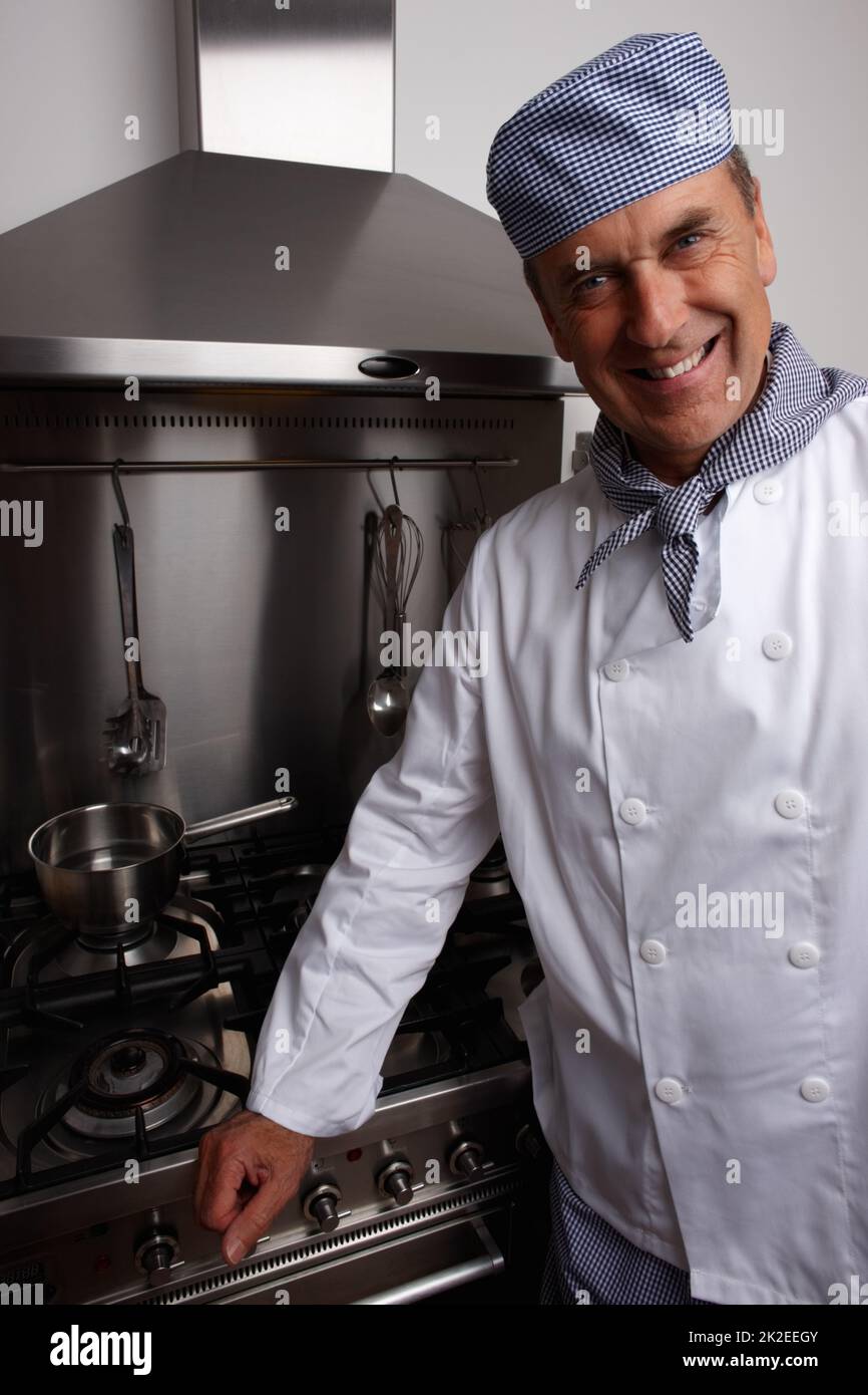 Sorridente chef senior in piedi da stufa a gas e cappa di ventilazione. Ritratto di uno chef sorridente in piedi da stufa a gas e cappa di ventilazione. Foto Stock