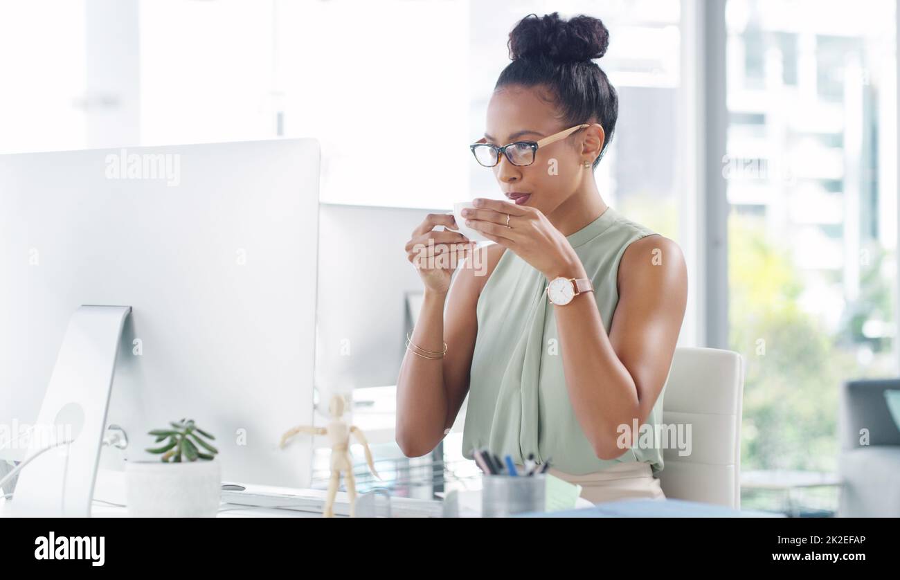 Avere se stessa un po 'di pausa caffè in ufficio. Immagine di una giovane e attraente donna d'affari che ha una tazza di caffè mentre lavora alla sua scrivania in un ufficio moderno. Foto Stock