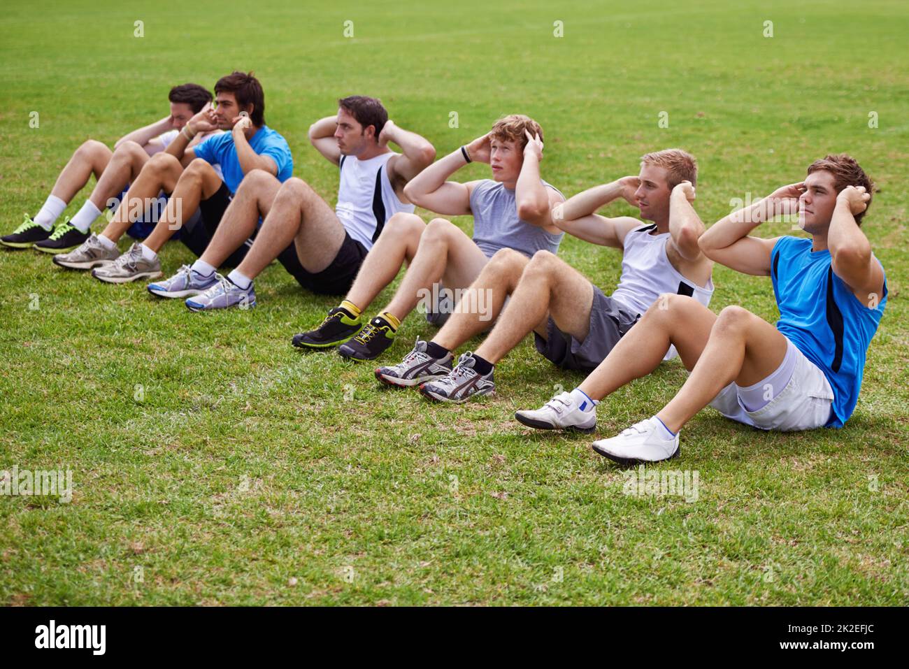 Muscoli addominali di acciaio. Shot di una fila di giovani sportivi che fanno sit-up. Foto Stock