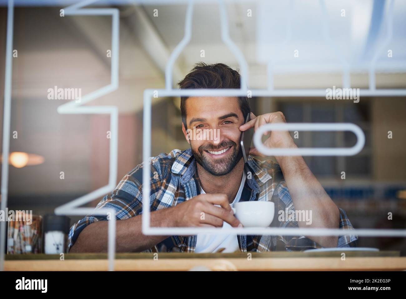 Rimanere in contatto durante la pausa caffè. Ritratto di un giovane felice che risponde al suo cellulare mentre si fa un caffè al suo caffè preferito. Foto Stock