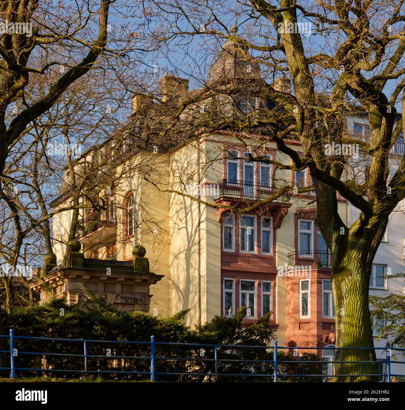 Vecchi edifici colorati accanto a un piccolo tempio nella città di Offenbach incorniciato da alberi, ringhiera blu di fronte Foto Stock