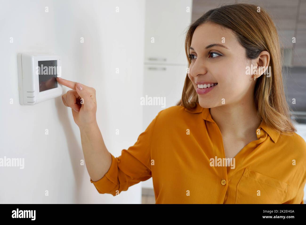 Ritratto di donna sorridente abbassa la temperatura sul termostato digitale a casa. Risparmio energetico, tecnologia efficiente e intelligente. Foto Stock
