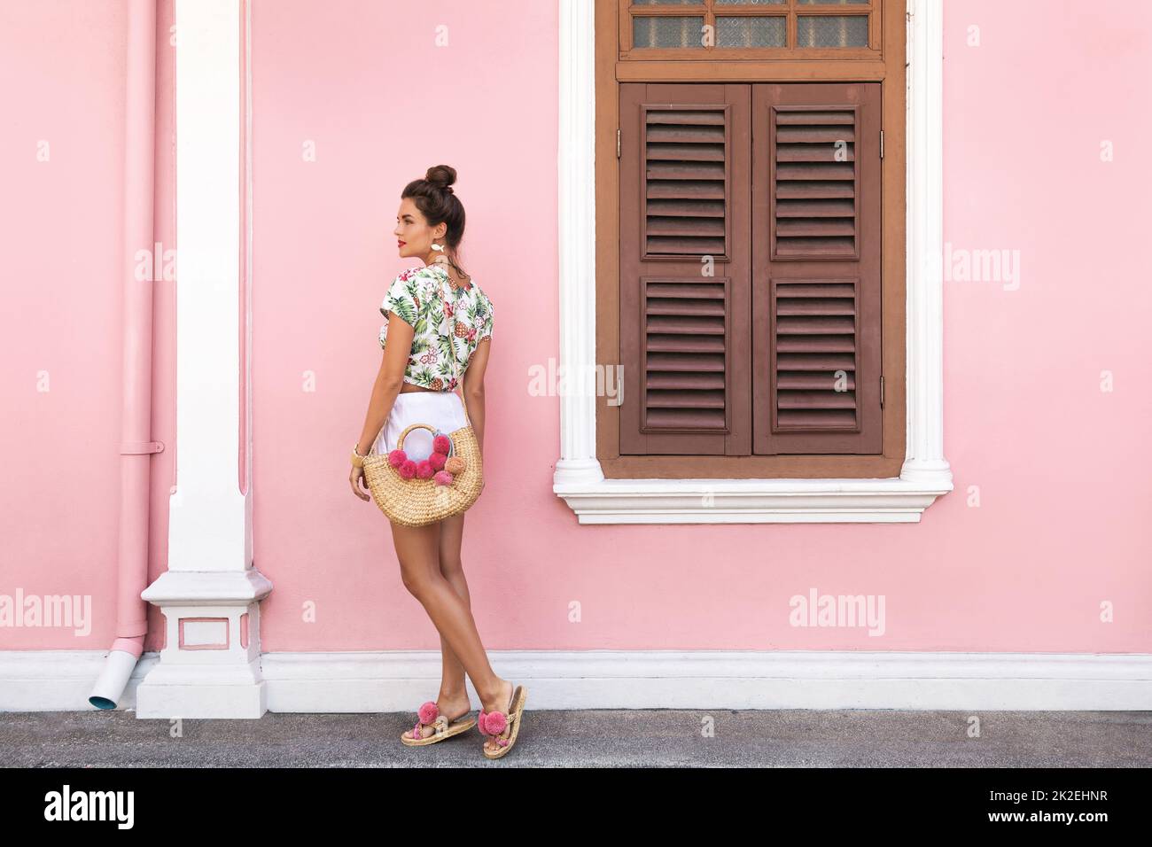 Bella e elegante donna in posa accanto alla casa con un muro rosa Foto Stock