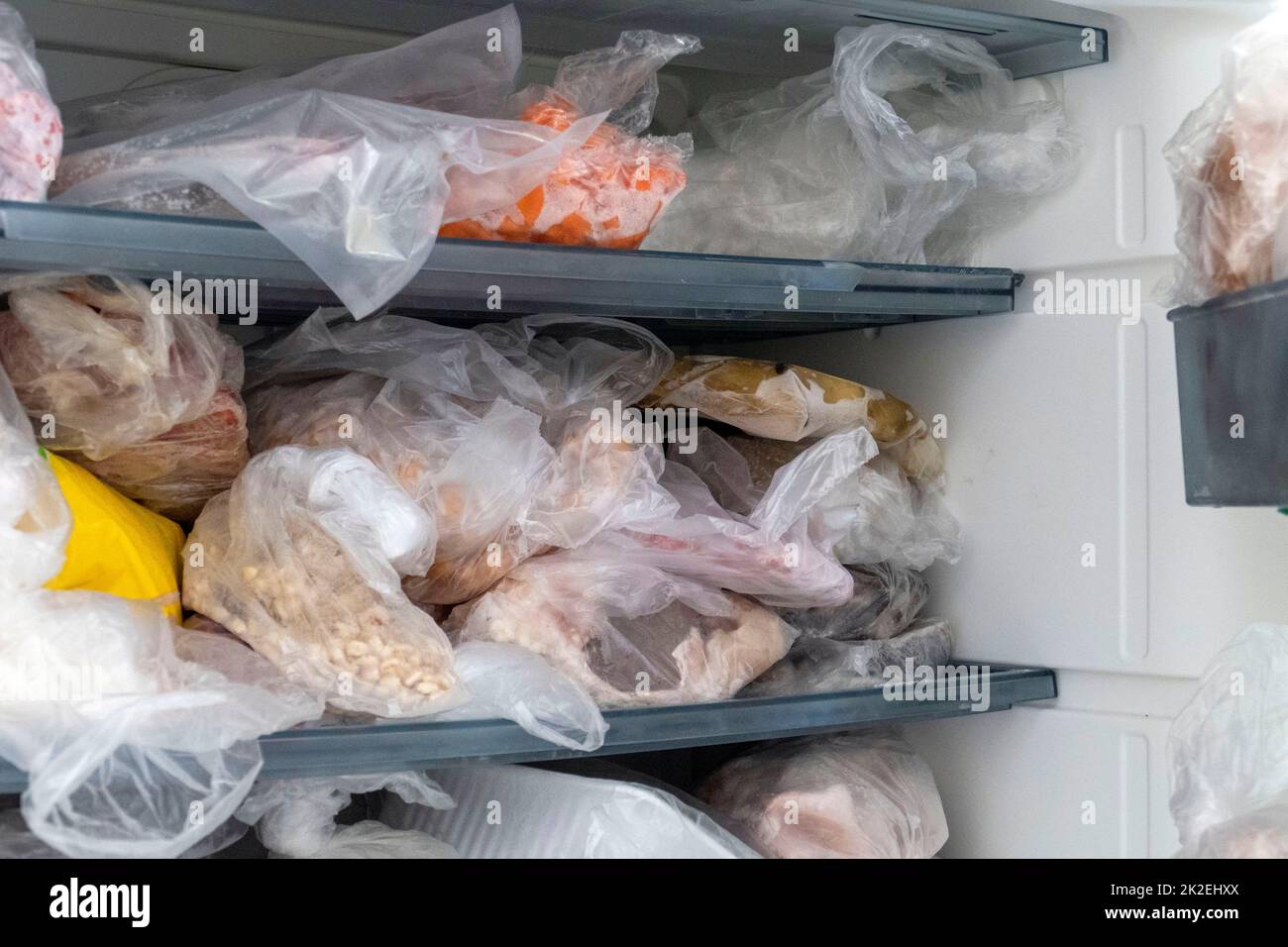Gli alimenti congelati sono in un congelatore con la porta aperta, un disordinato all'interno di un congelatore profondo Foto Stock