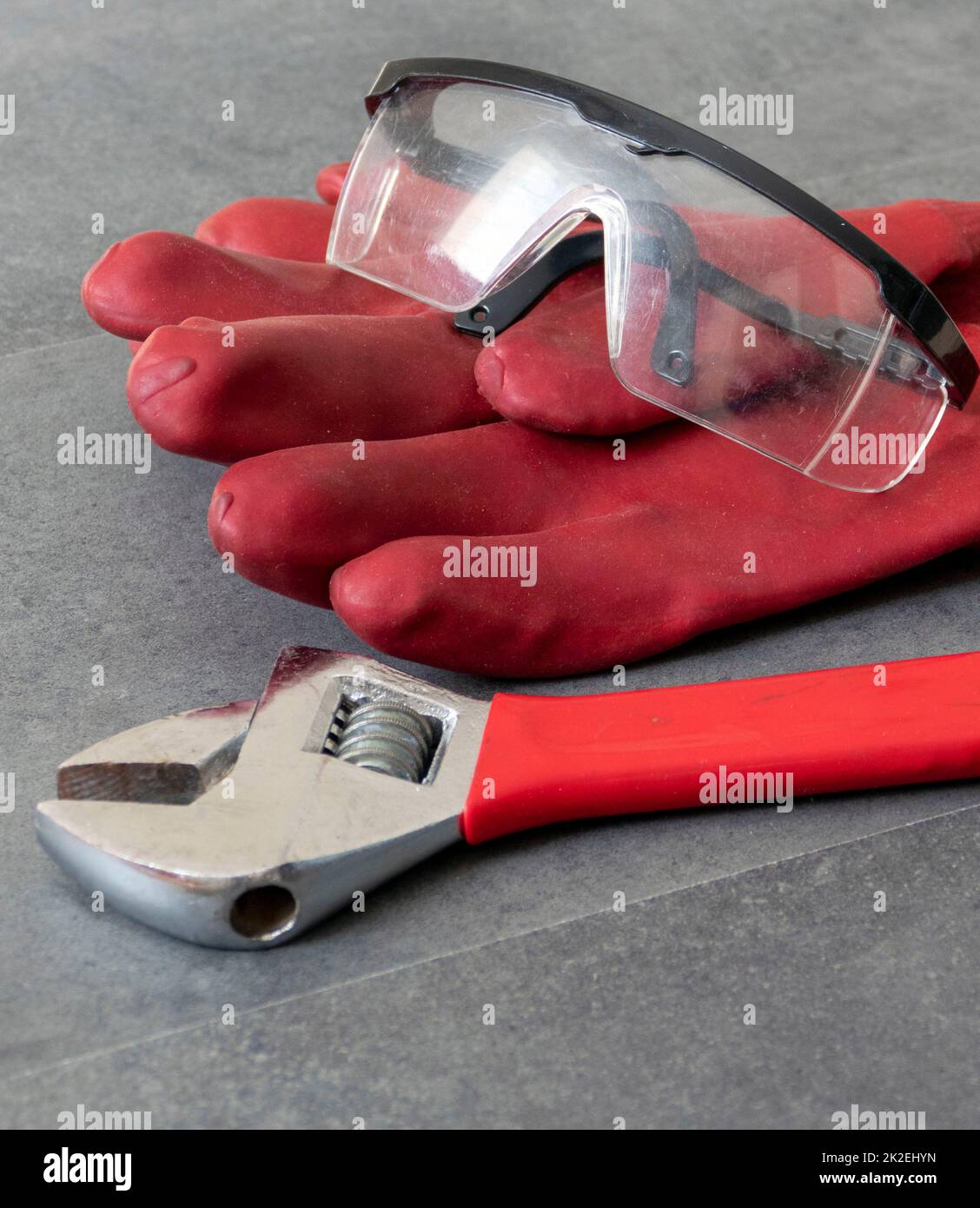 Per la sicurezza sul lavoro, è necessario lavorare con guanti, occhiali protettivi, una chiave su un pavimento, guanti in plastica spessi e occhiali protettivi Foto Stock