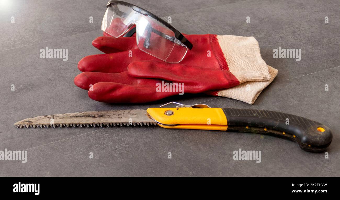 per la sicurezza sul lavoro, è necessario lavorare con i guanti, c'è una sega a mano e guanti di plastica spessi su un pavimento Foto Stock
