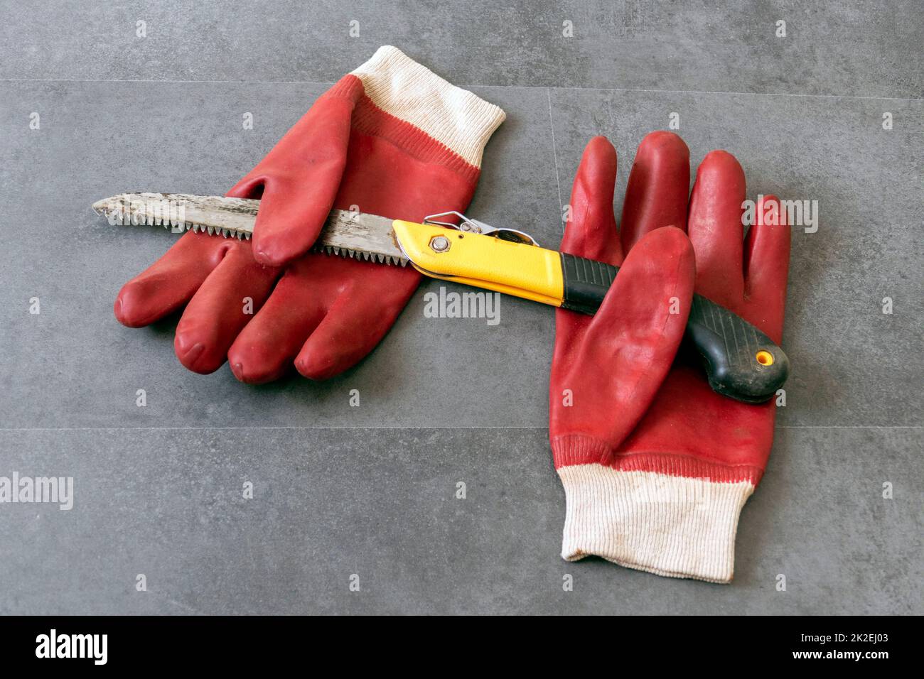 per la sicurezza sul lavoro, è necessario lavorare con i guanti, c'è una sega a mano e guanti di plastica spessi su un pavimento Foto Stock