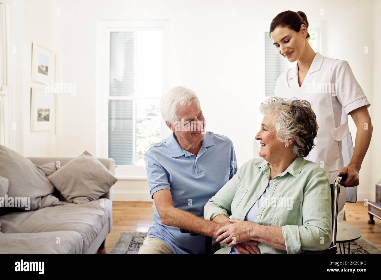 Assicurandosi che i ceneri bene curati dopo. Girato di un caregiver sorridente con una donna anziana in sedia a rotelle e suo marito a casa. Foto Stock