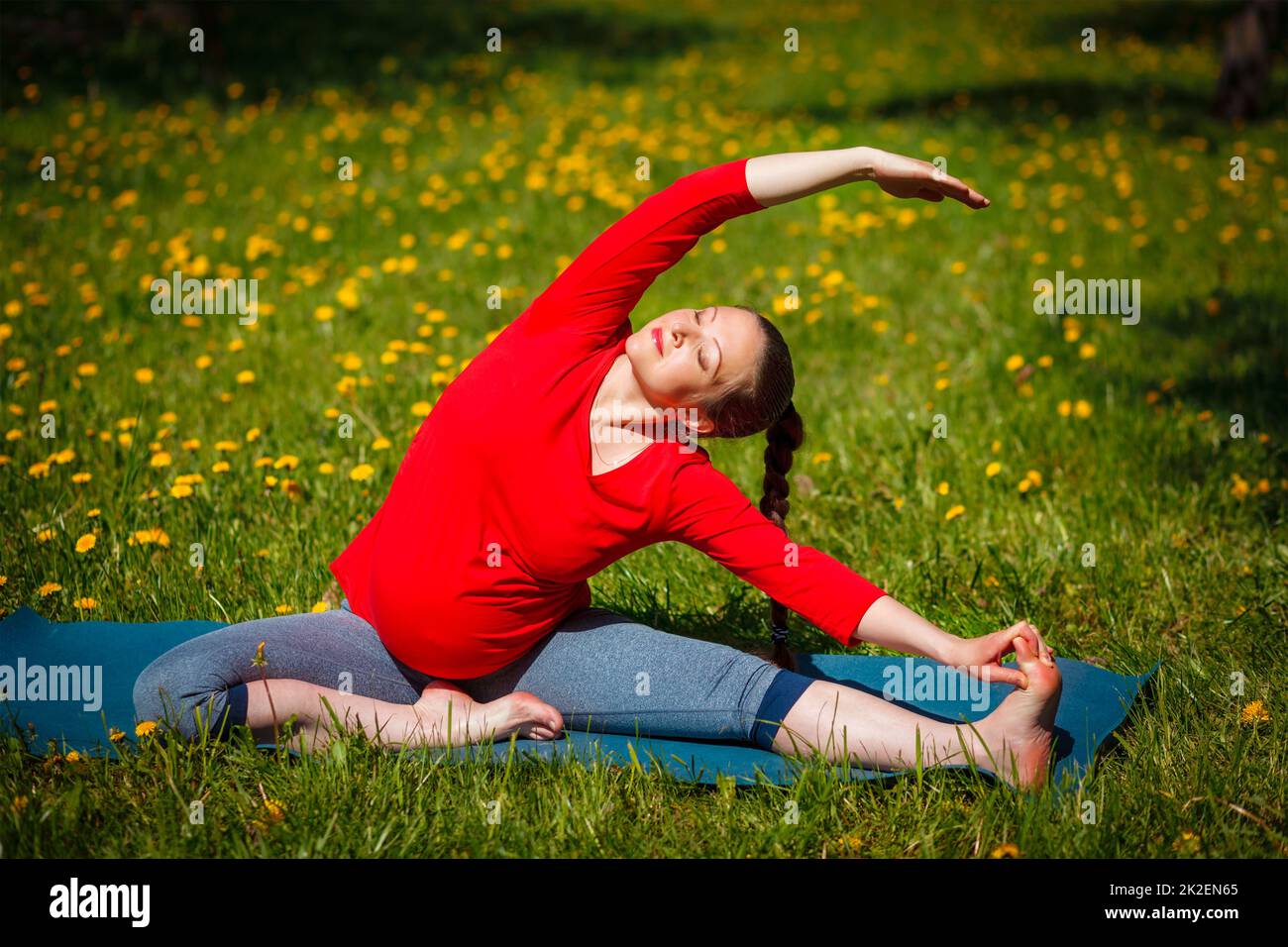 Donna incinta che fa asana Parivrtta Janu Sirsasana all'aperto Foto Stock