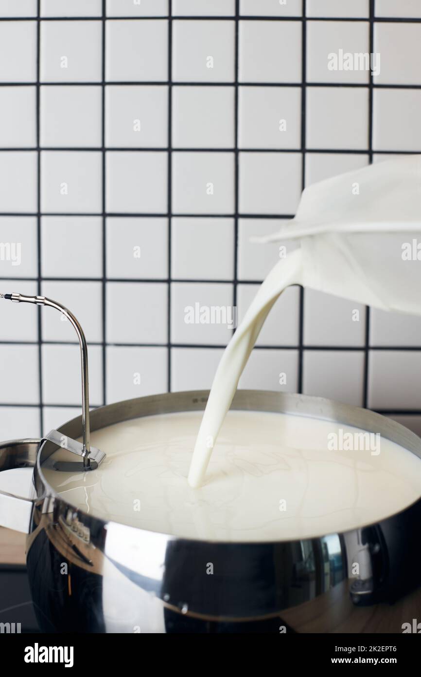 Il processo di preparazione dello yogurt fatto in casa. Il latte viene versato in un contenitore per il riscaldamento. Foto verticale. Foto Stock