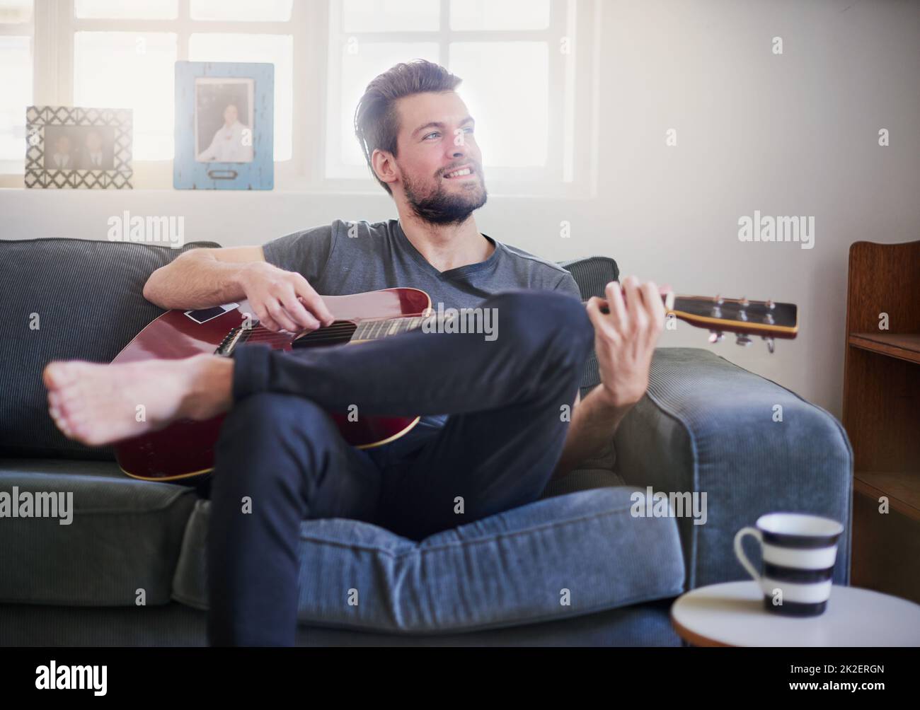 Ascoltare la musica, levigare la mente. Scatto corto di un bel giovane che suona una chitarra a casa. Foto Stock