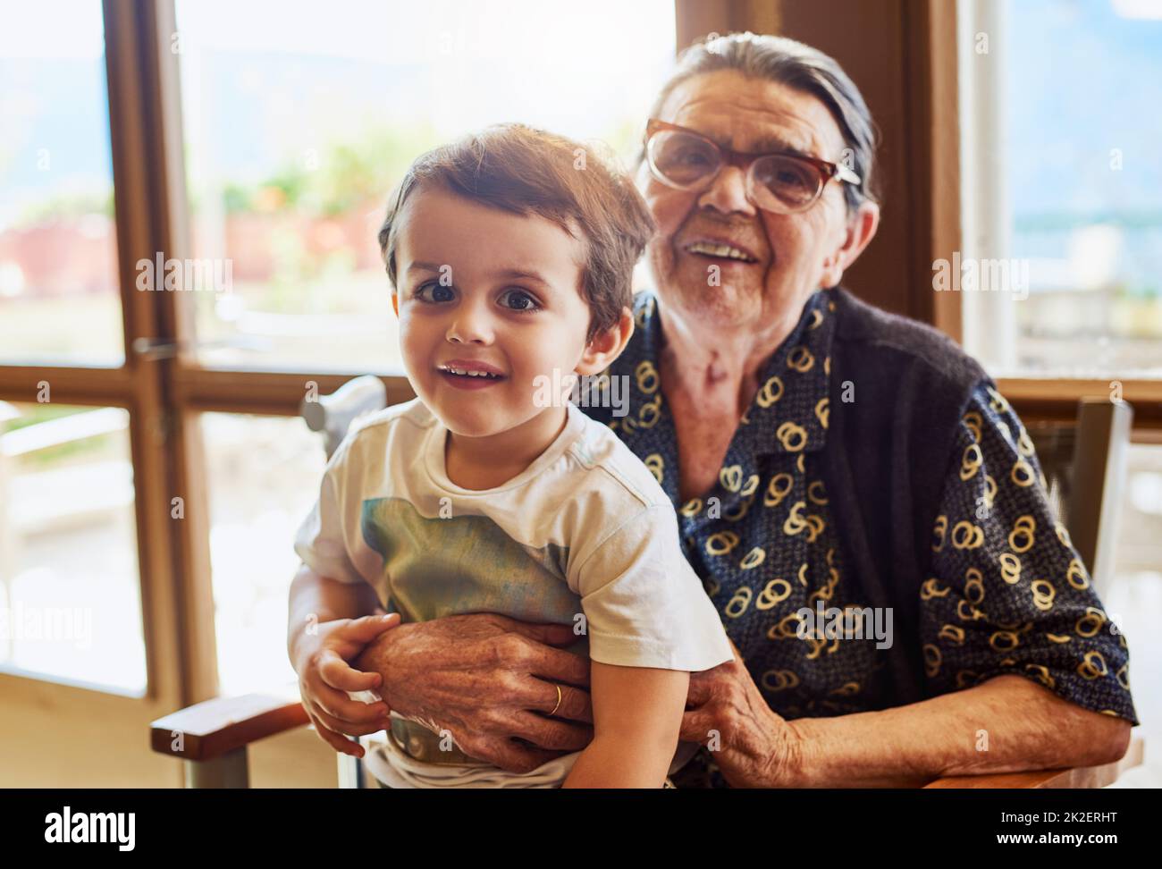 Il più antico e il più giovane della famiglia. Ritratto di un ragazzino allegro seduto sul suo grembo di nonne mentre guarda la macchina fotografica a casa. Foto Stock