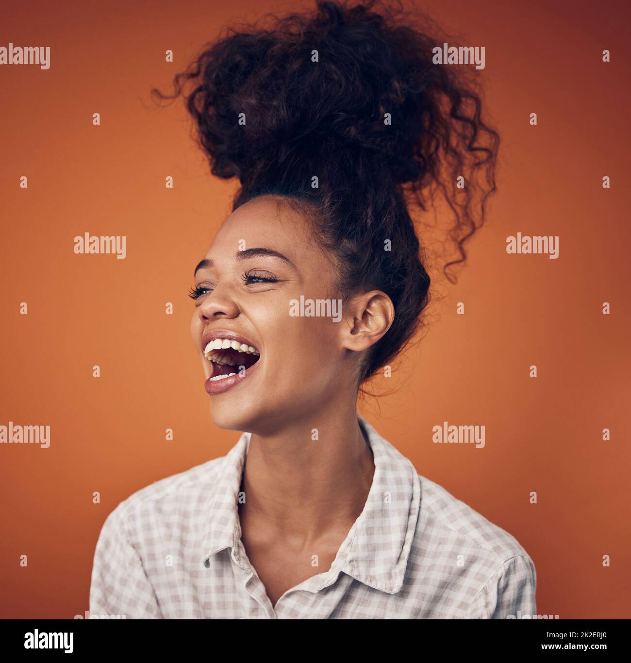 Non riesco a smettere di ridere. Scatto di una giovane donna che indossa i capelli in una pistola contro uno sfondo arancione. Foto Stock