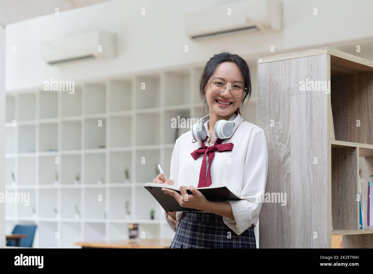 Giovane studentessa che svolge compiti in biblioteca. Donna asiatica che prende appunti dai libri di testo. Foto Stock