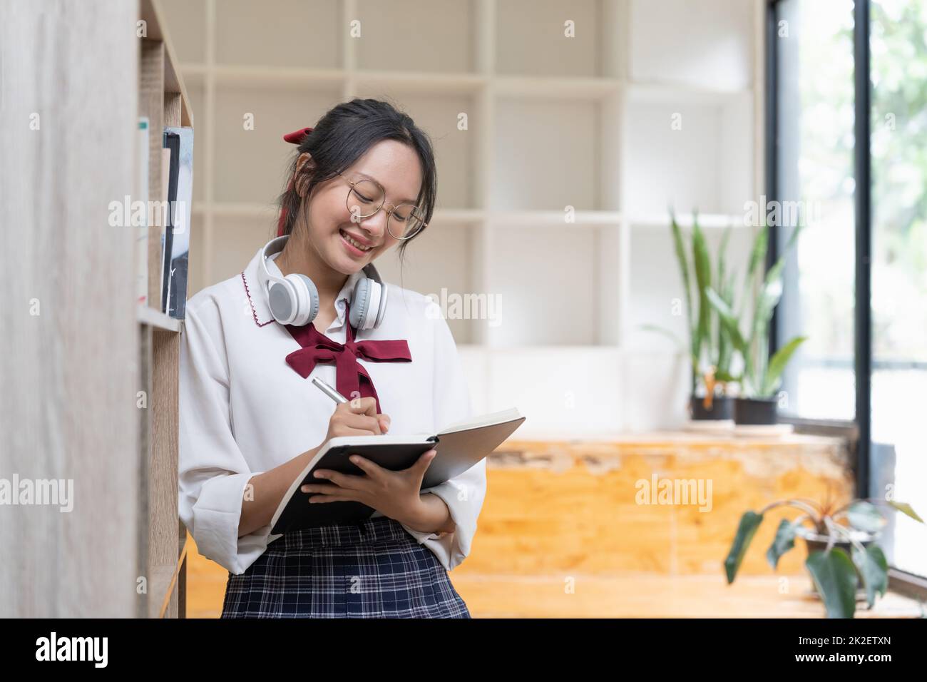 Giovane studentessa che svolge compiti in biblioteca. Donna asiatica che prende appunti dai libri di testo. Foto Stock