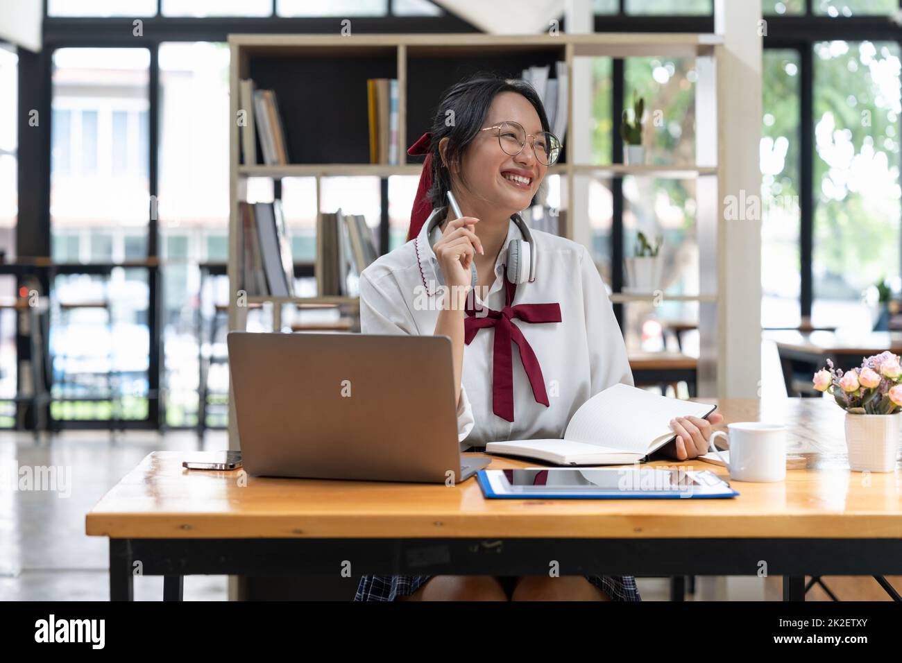 Donna asiatica sorridente prende appunti guardando i webinar sul laptop, cercando attività aziendali, uno studente maschile sta studiando online, ascoltando video Foto Stock