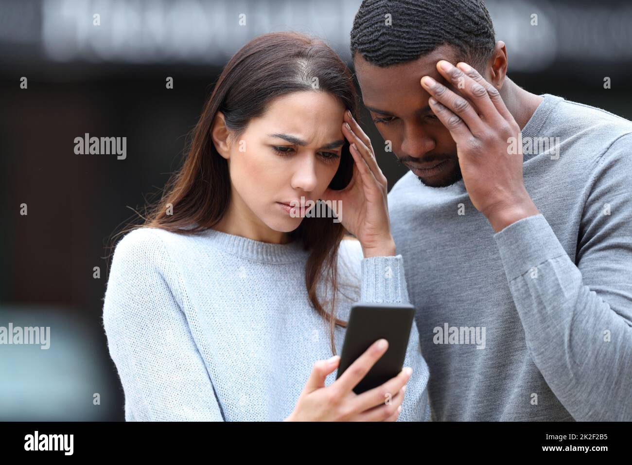 Preoccupata coppia interracial che controlla il telefono nella strada Foto Stock