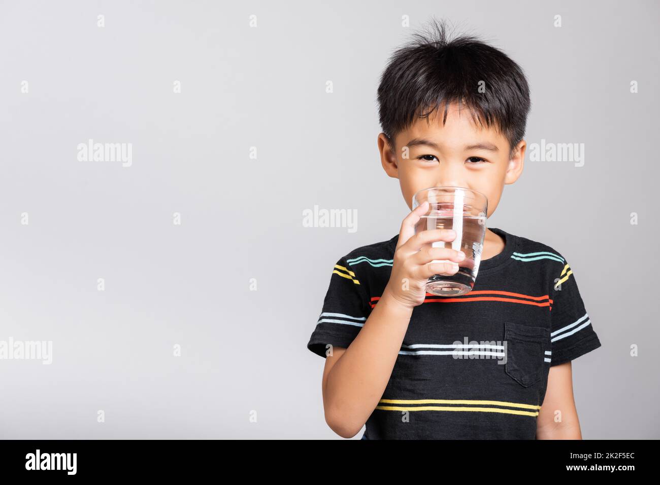 Bambino piccolo carino ragazzo di 5-6 anni sorriso bere acqua fresca dal vetro in studio ripresa isolato Foto Stock