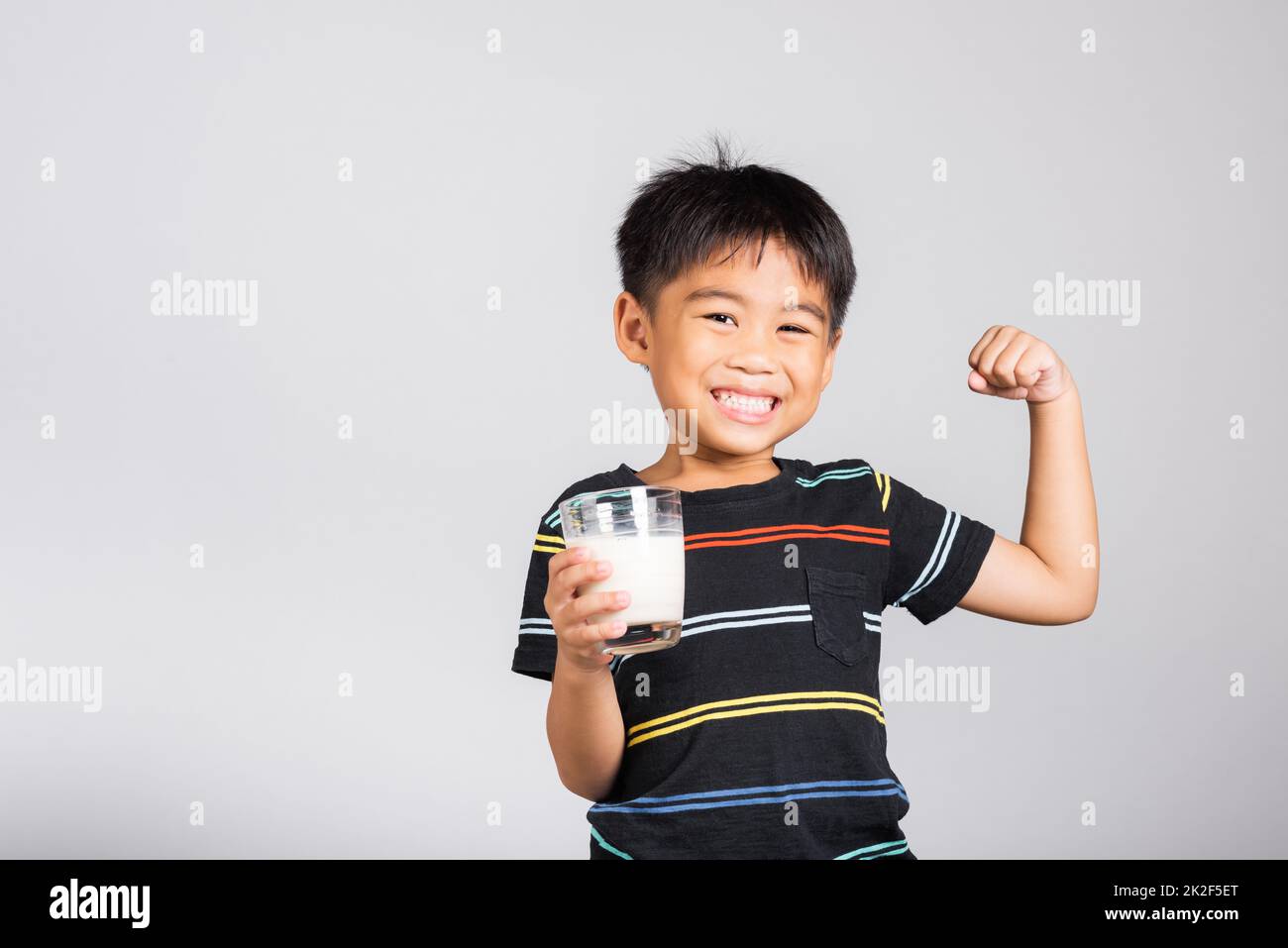 Piccolo ragazzo carino di 5-6 anni sorride tenendo il bicchiere di latte e mostrare il potere forte gesto Foto Stock