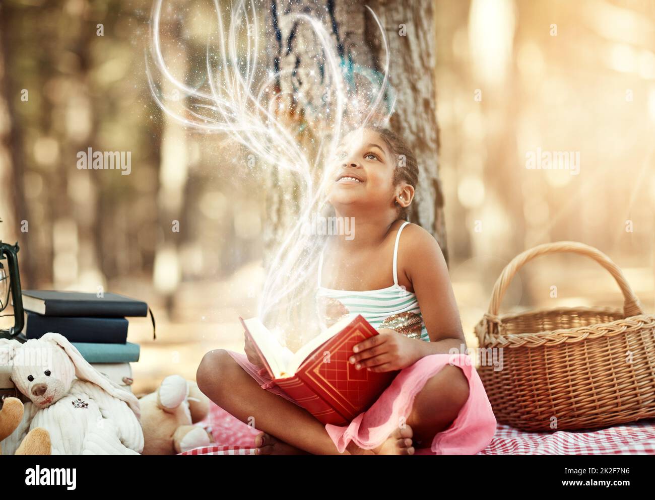 Apri un libro e apri la tua mente. Scatto di una bambina che legge un libro con i suoi giocattoli nei boschi. Foto Stock