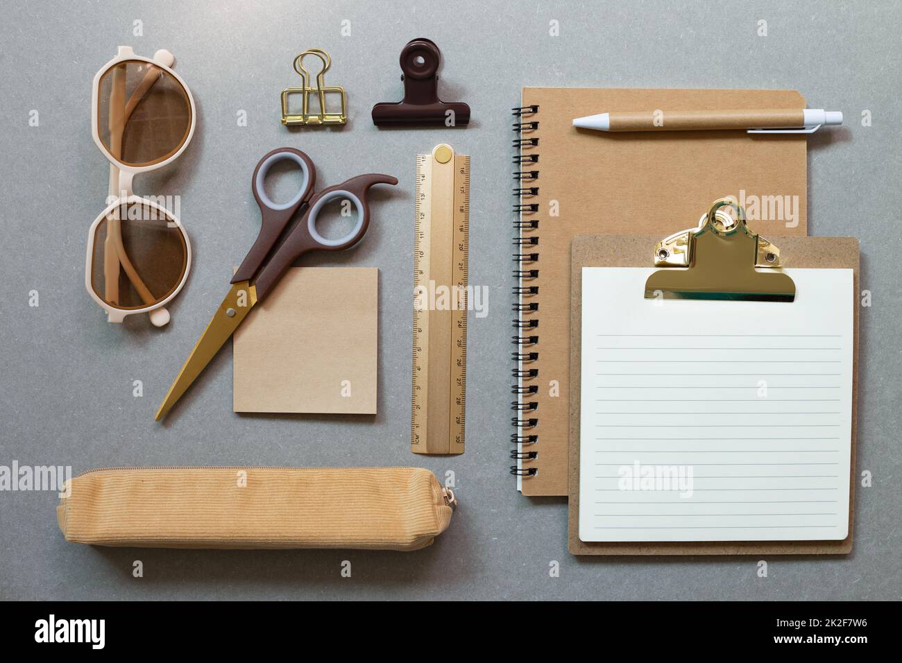 Notebook marrone, appunti, penna, righello, clip, blocco note, custodia per matita, forbici, occhiali su sfondo grigio da scrivania. materiale per ufficio da lavoro. piatto, t Foto Stock