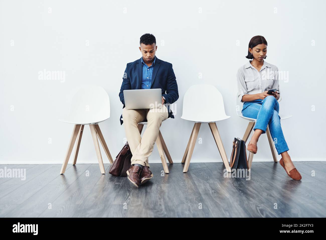 Fare rapidamente i preparativi finali prima della grande presentazione. Immagine a tutta lunghezza di due giovani uomini d'affari seduti sulle sedie e utilizzando i loro dispositivi tecnologici su uno sfondo grigio. Foto Stock