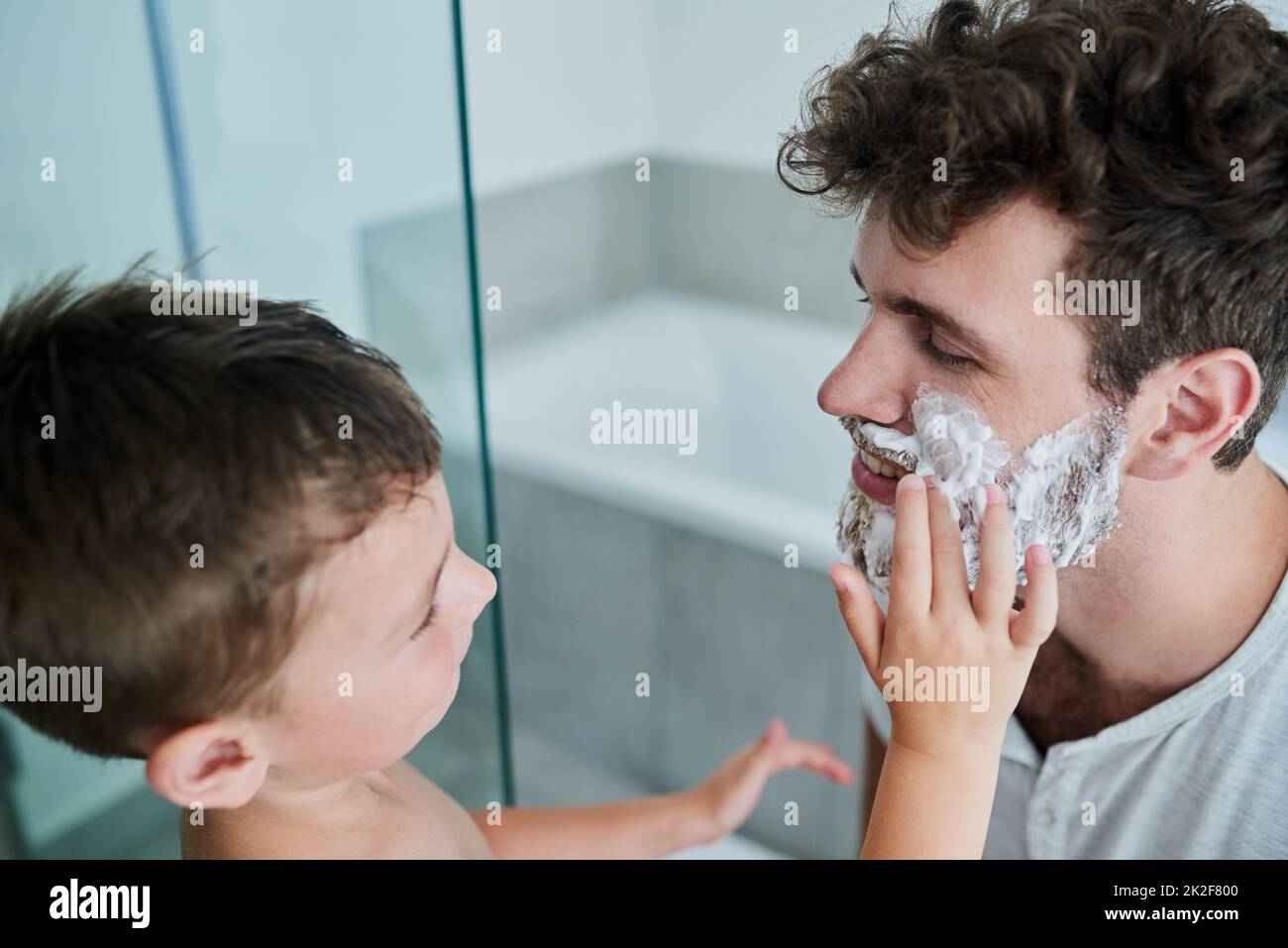 Lascilo fare esso per voi papà. Shot di un bambino strofinando crema di rasatura sul viso dei padri nel bagno di casa. Foto Stock
