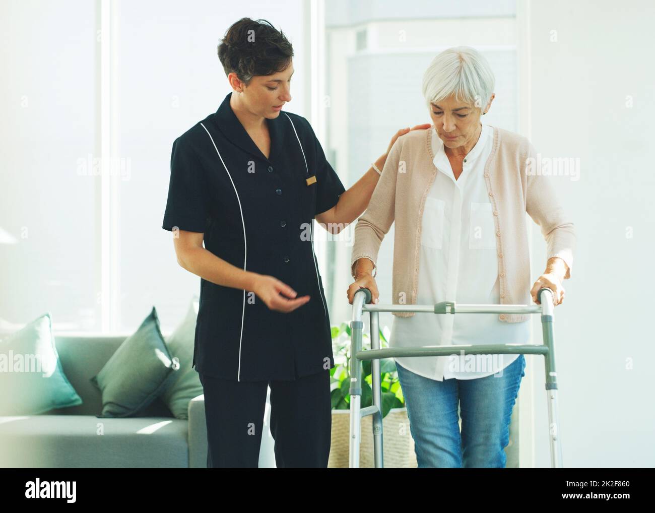 Stai facendo molto bene. Scatto corto di un professionista giovane attraente di sanità che aiuta il suo paziente anziano a camminare con un camminatore in una casa di cura. Foto Stock