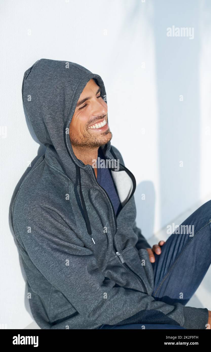 Felice di ritrovarsi. Un bel ragazzo seduto sul pavimento e sorridente indossando una felpa con cappuccio. Foto Stock