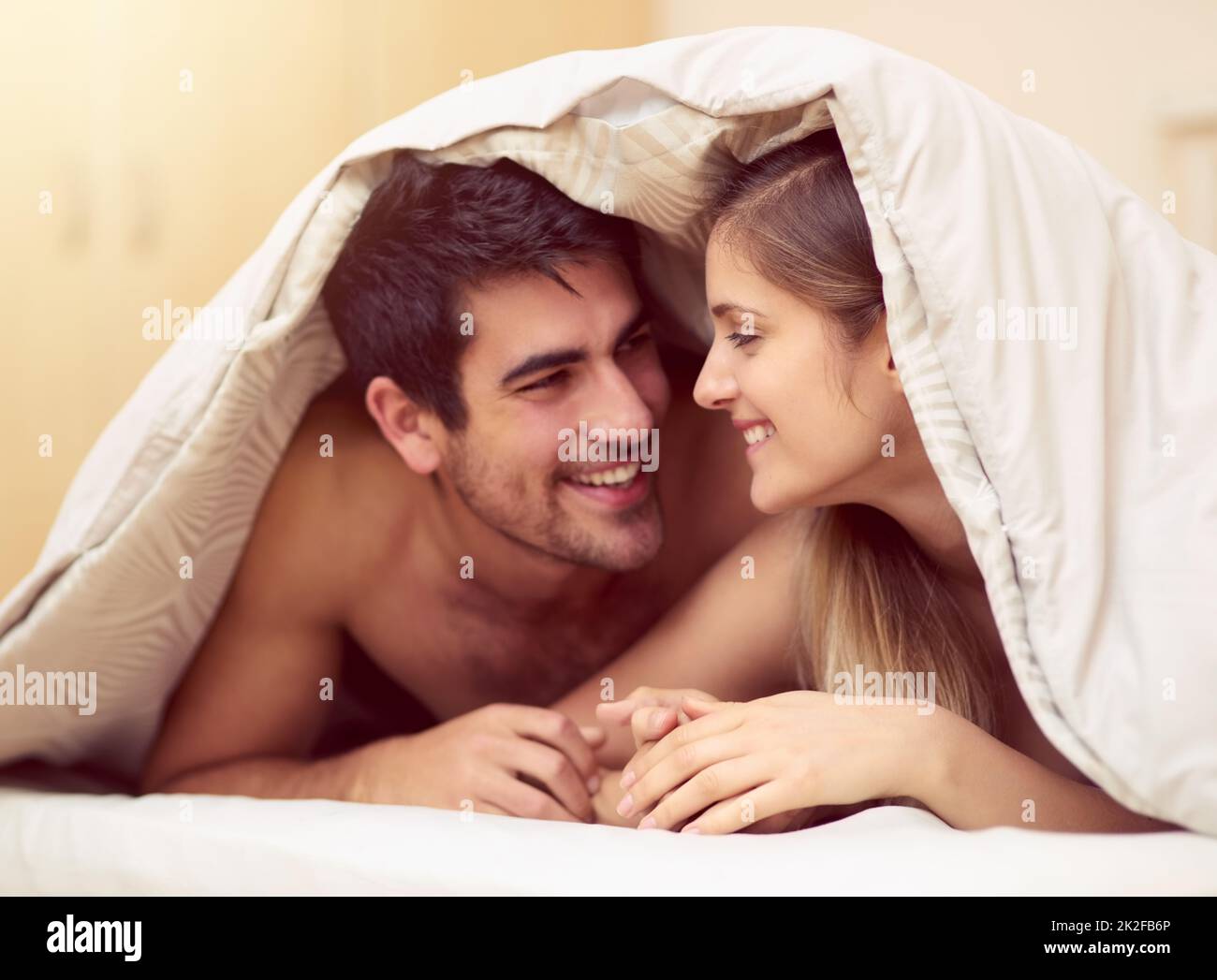 Ami quello con cui sei. Scatto di una giovane coppia amorevole che sorride l'un l'altro mentre si trova sotto una coperta insieme. Foto Stock
