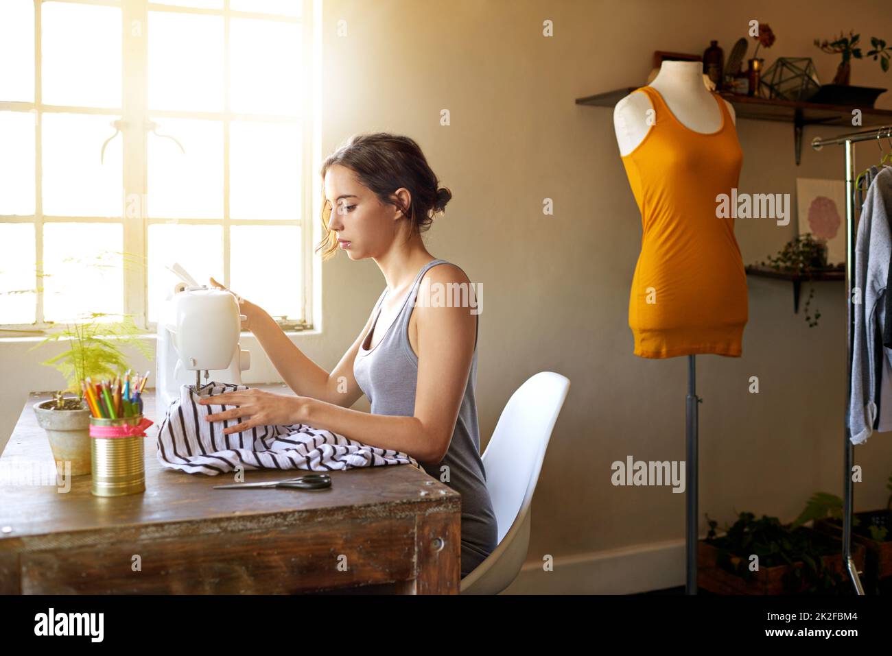 Ogni giorno speso cucire è un Buon giorno. Un giovane designer che fa un abito sul suo posto di lavoro. Foto Stock