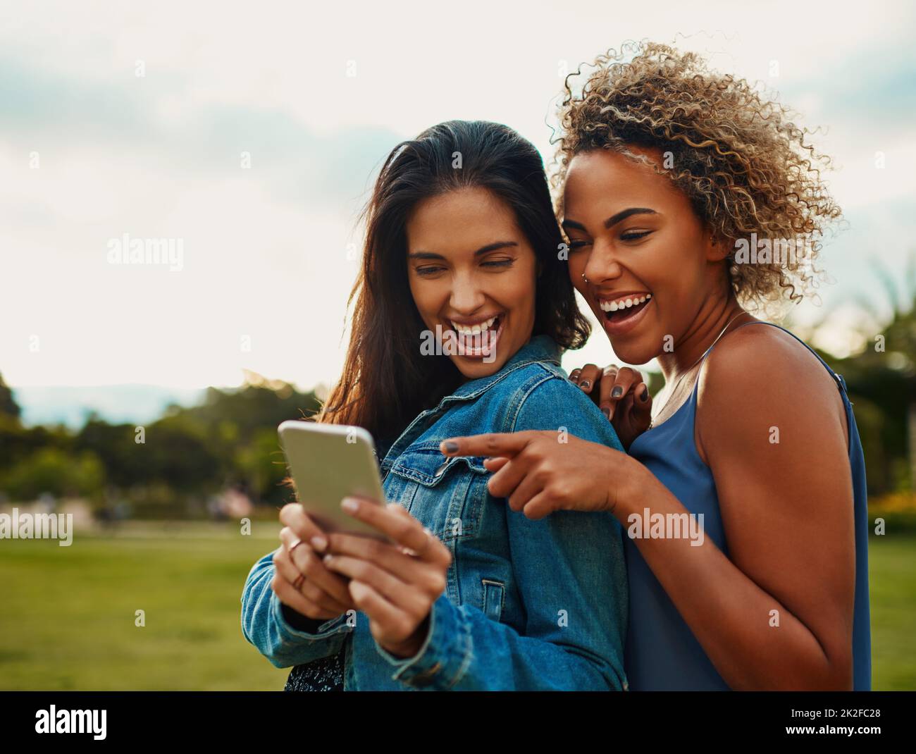 Questa è l'app di cui stavo parlando. Scatto corto di due giovani amiche attraenti usando uno smartphone insieme mentre si trova in un parco. Foto Stock