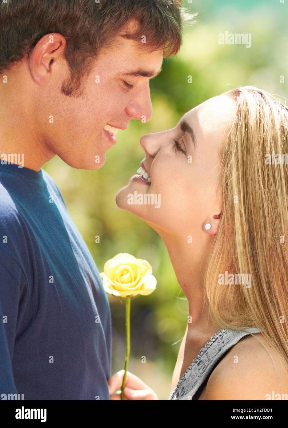 L'amore fiorisce. Una coppia giovane che guarda amorevolmente l'un l'altro mentre la donna tiene un fiore. Foto Stock