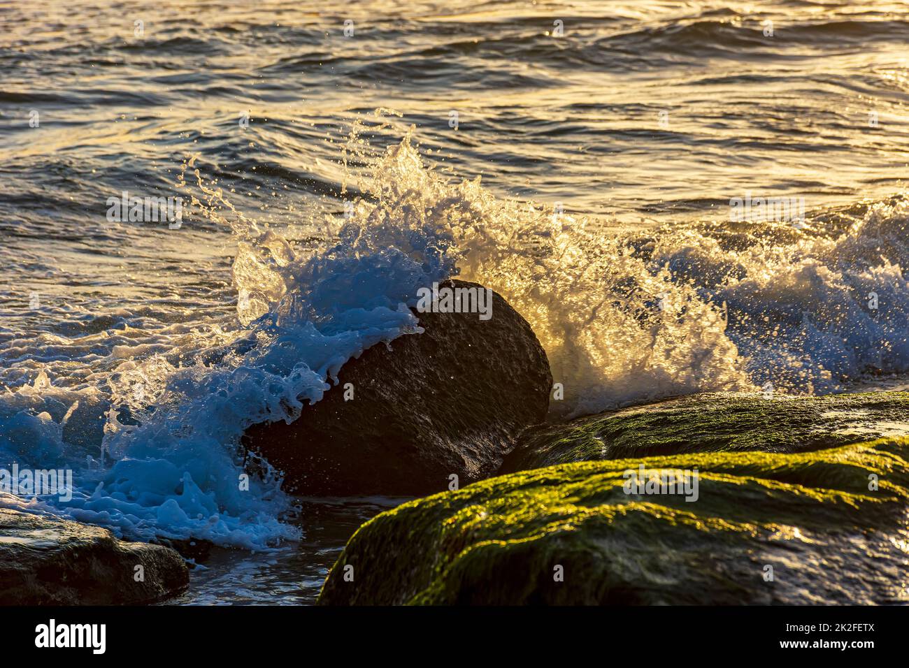 Acqua e schiuma di mare spruzzi al tramonto Foto Stock