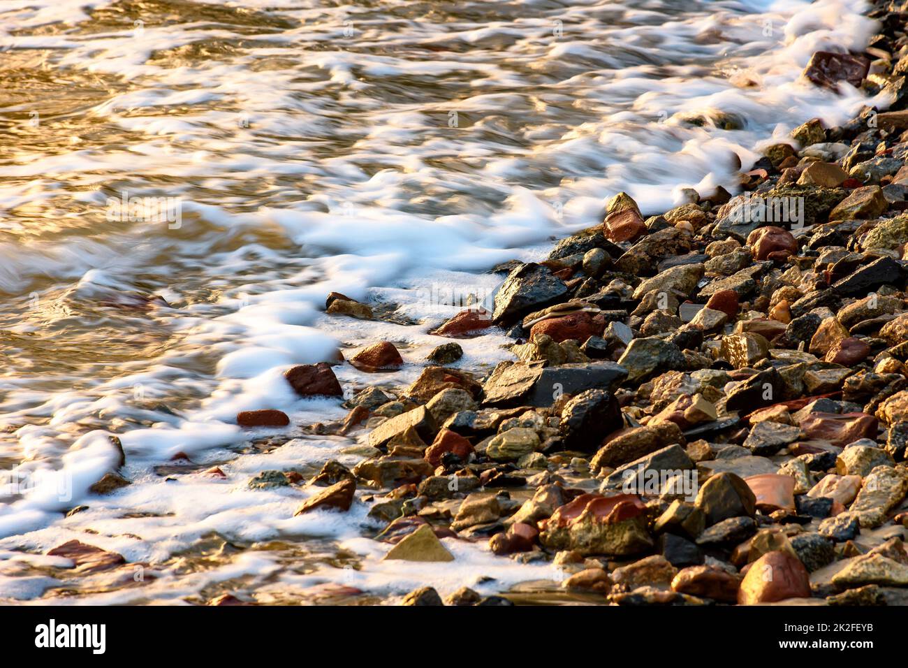 Piccole pietre sulla riva con la schiuma Foto Stock