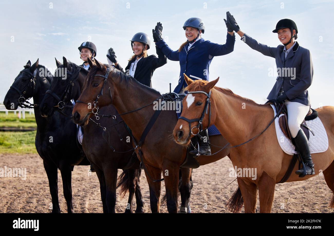 L'abbiamo fatto. Scatto corto di un gruppo di belle giovani jockey femmina high-fiving mentre si siede sulle loro spalle dei cavalli. Foto Stock