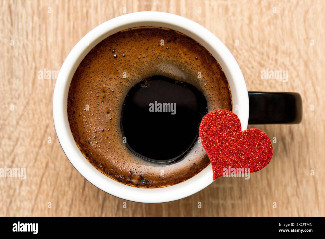 Piccolo cuore rosso fissato sul bordo di una tazza di ceramica con caffè nero Foto Stock