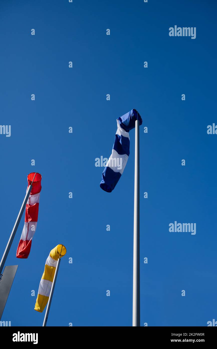 3 calze a vento in blu, giallo e rosso, su un cielo azzurro brillante di giorno, di giorno, di vento Foto Stock