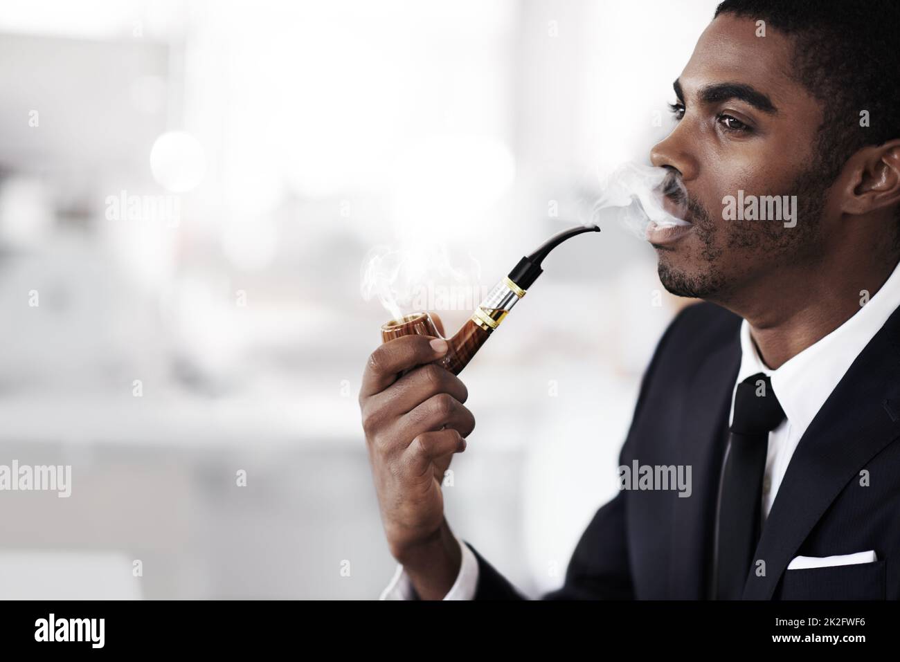 Godere di un fumo senza le impurità. Profilo di un giovane uomo d'affari che fuma una pipa elettronica in un ufficio. Foto Stock