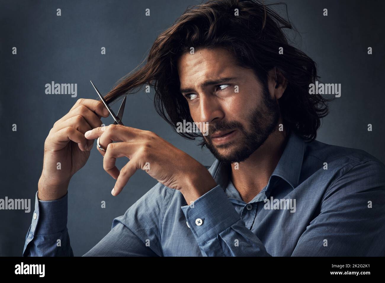 È il momento di tritare tutto. Studio girato di un bel giovane uomo tagliando i capelli su uno sfondo grigio. Foto Stock