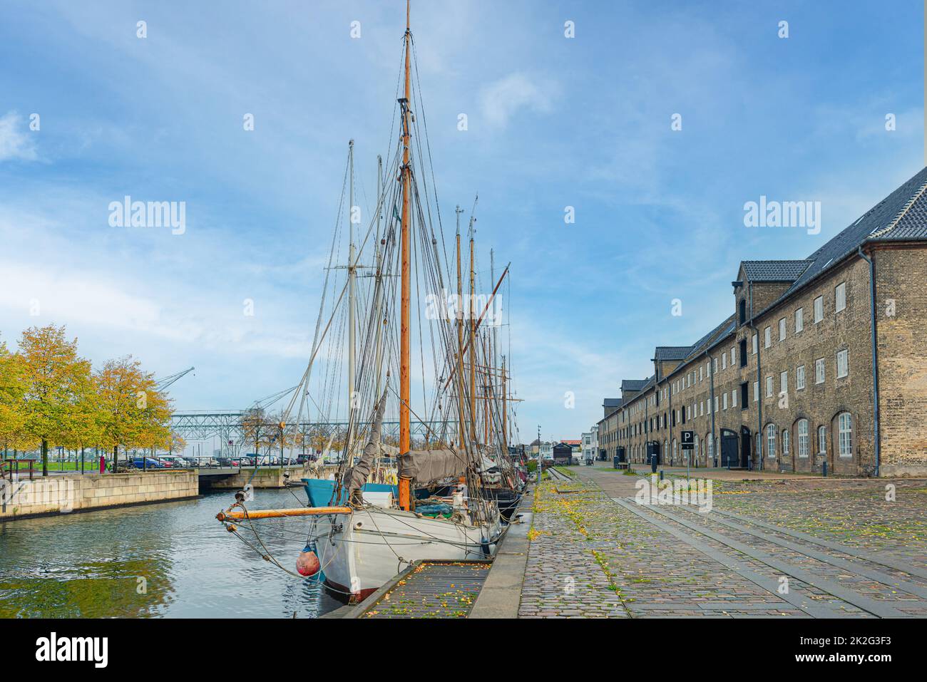Barche a vela con alberi in piedi sull'acqua del canale vicino a tre piani edifici in mattoni grigi su una strada con un pavimento in pietra Christianshavn.Copenhagen, Danimarca Foto Stock