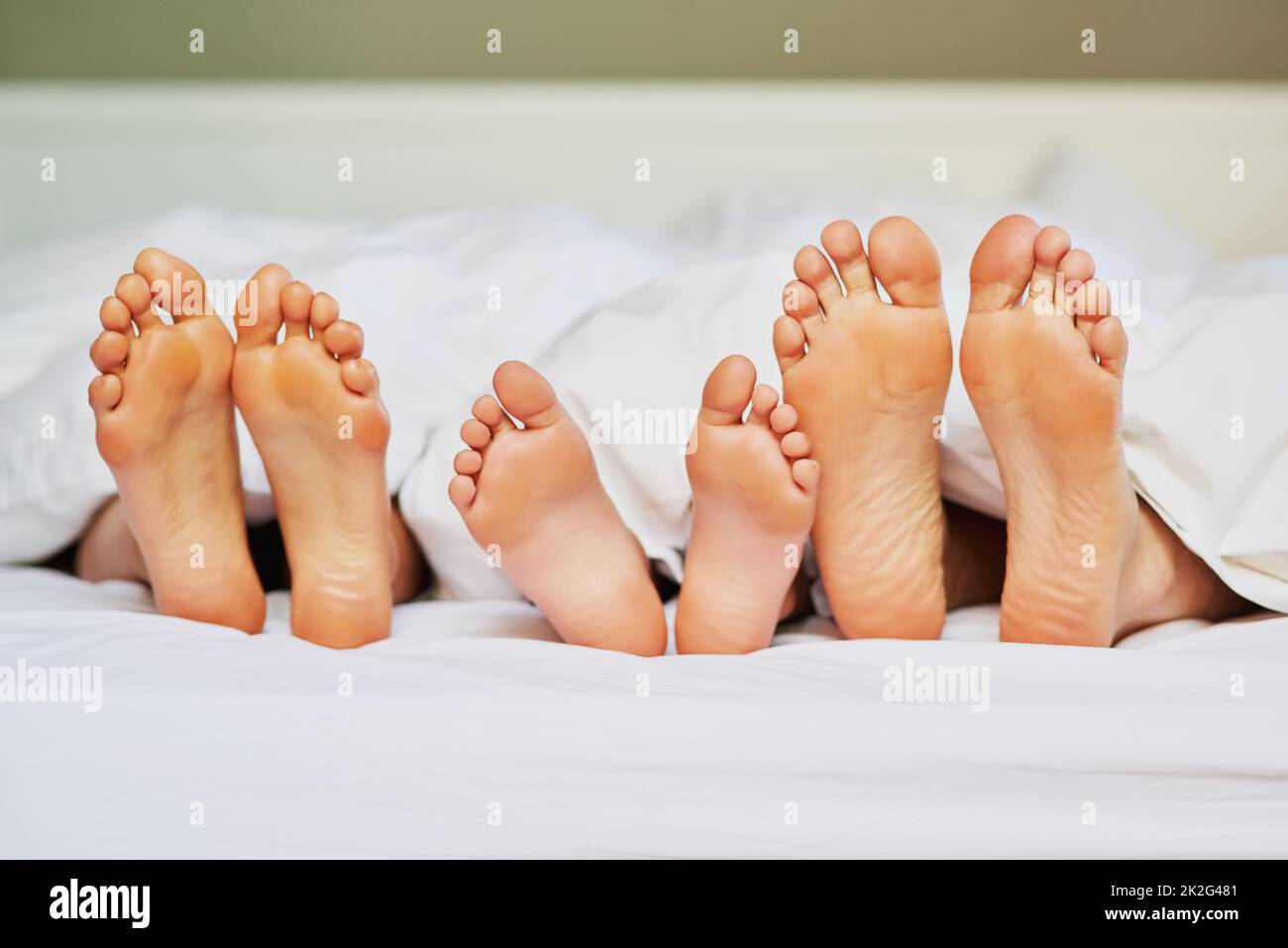 Tenere i piedi in alto. Shot di un irriconoscibile familys piedi posizionati l'uno accanto all'altro a letto mentre theyre dorme a casa al mattino. Foto Stock