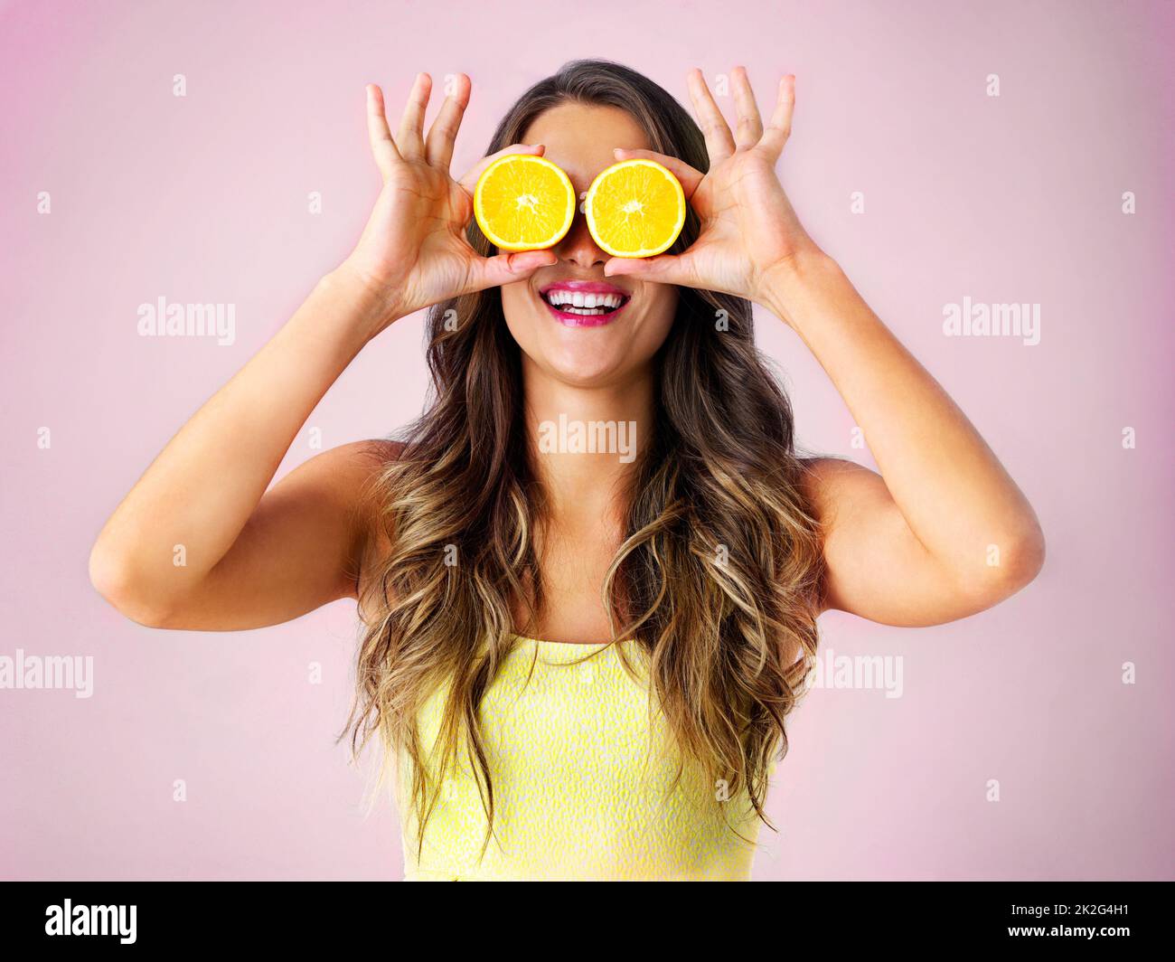 Guardate il lato luminoso. Studio girato di una giovane donna che tiene due metà di un arancione davanti ai suoi occhi. Foto Stock