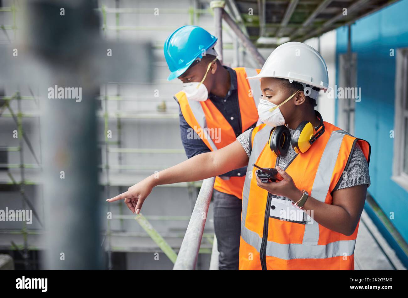 Scalatura di nuove altezze nel settore delle costruzioni. Scatto di una giovane donna con un walkie talkie mentre lavora con il suo collega in un cantiere. Foto Stock