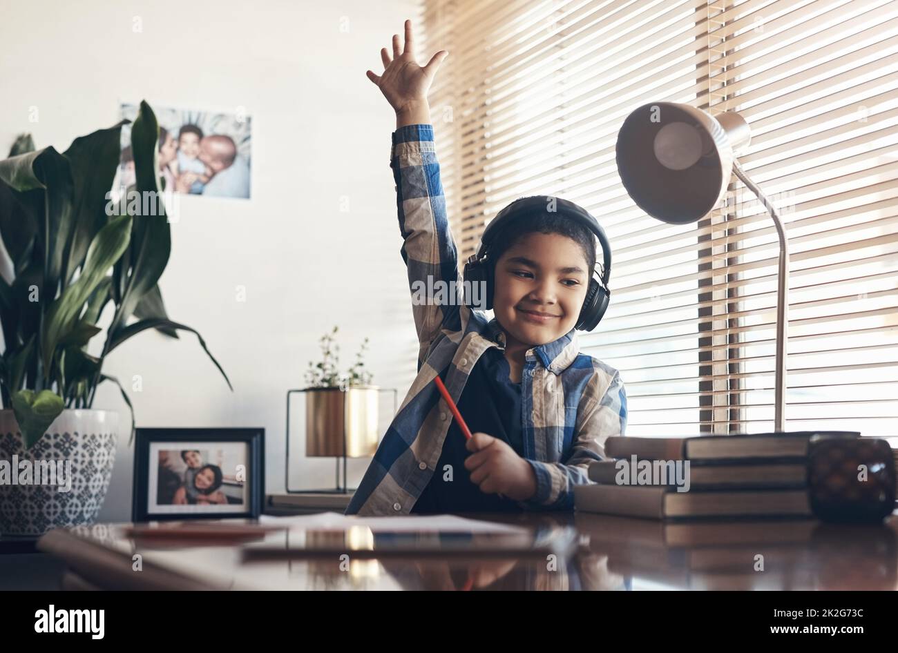 L'apprendimento non si ferma mai, nemmeno in blocco. Ripresa di un adorabile ragazzino con le cuffie e sollevando la mano mentre completava un'attività scolastica a casa. Foto Stock