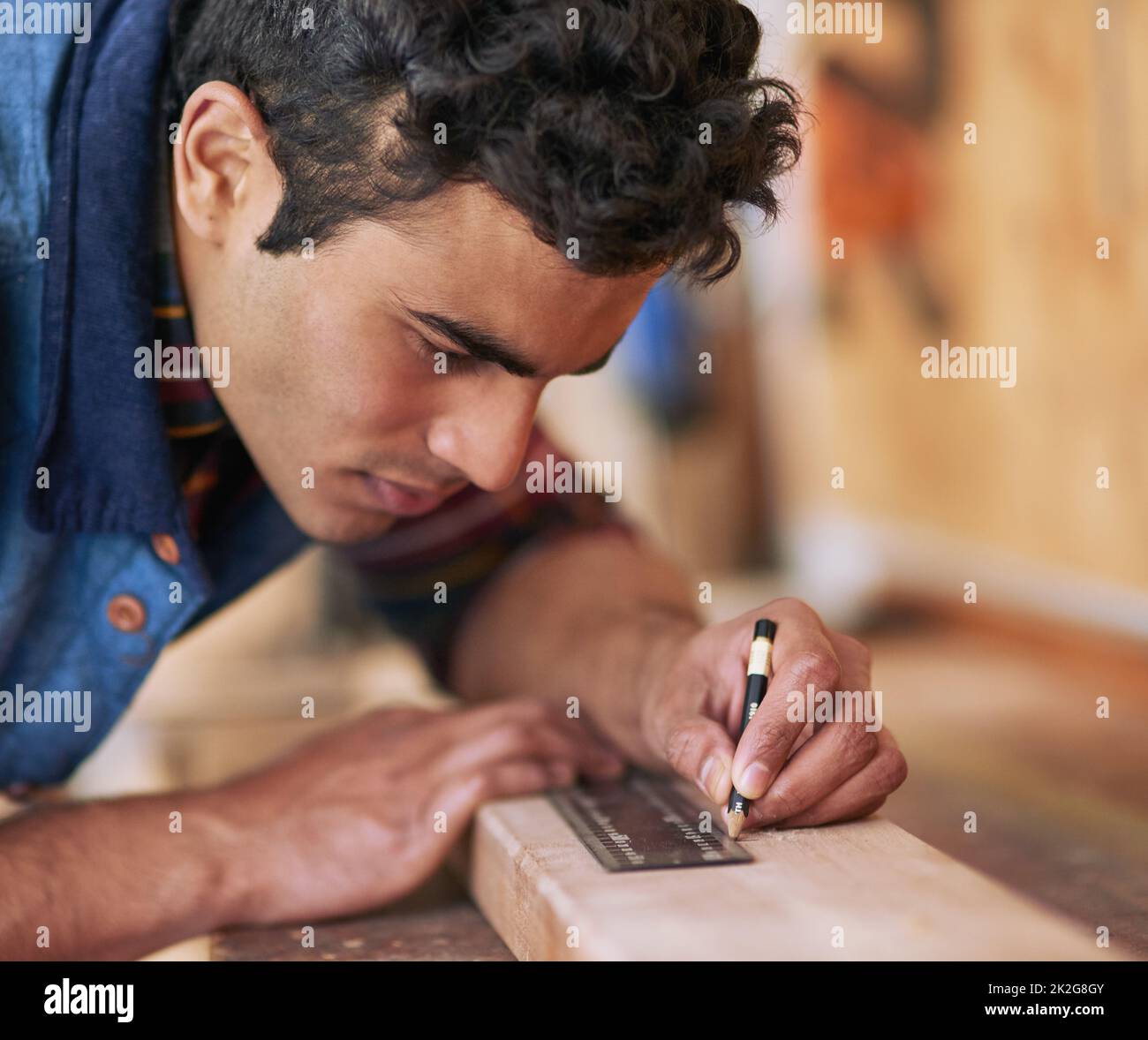 La prima volta. Scatto di un handyman focalizzato che misura un pezzo di legno mentre lavora nella sua officina. Foto Stock
