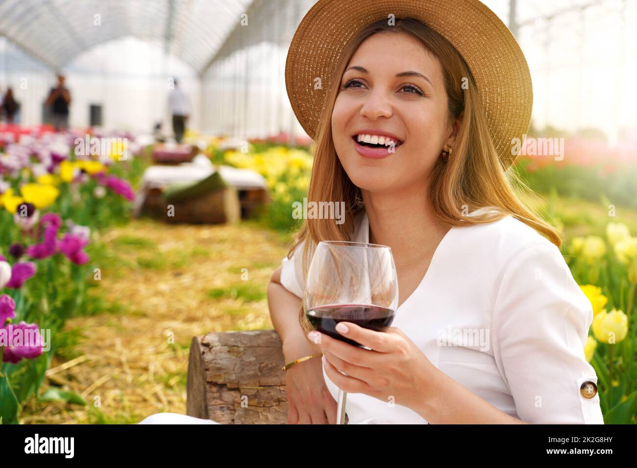 Immagine di una donna luminosa che si siede tra i fiori in giardino bar esterno che tiene il bicchiere di vino in primavera Foto Stock