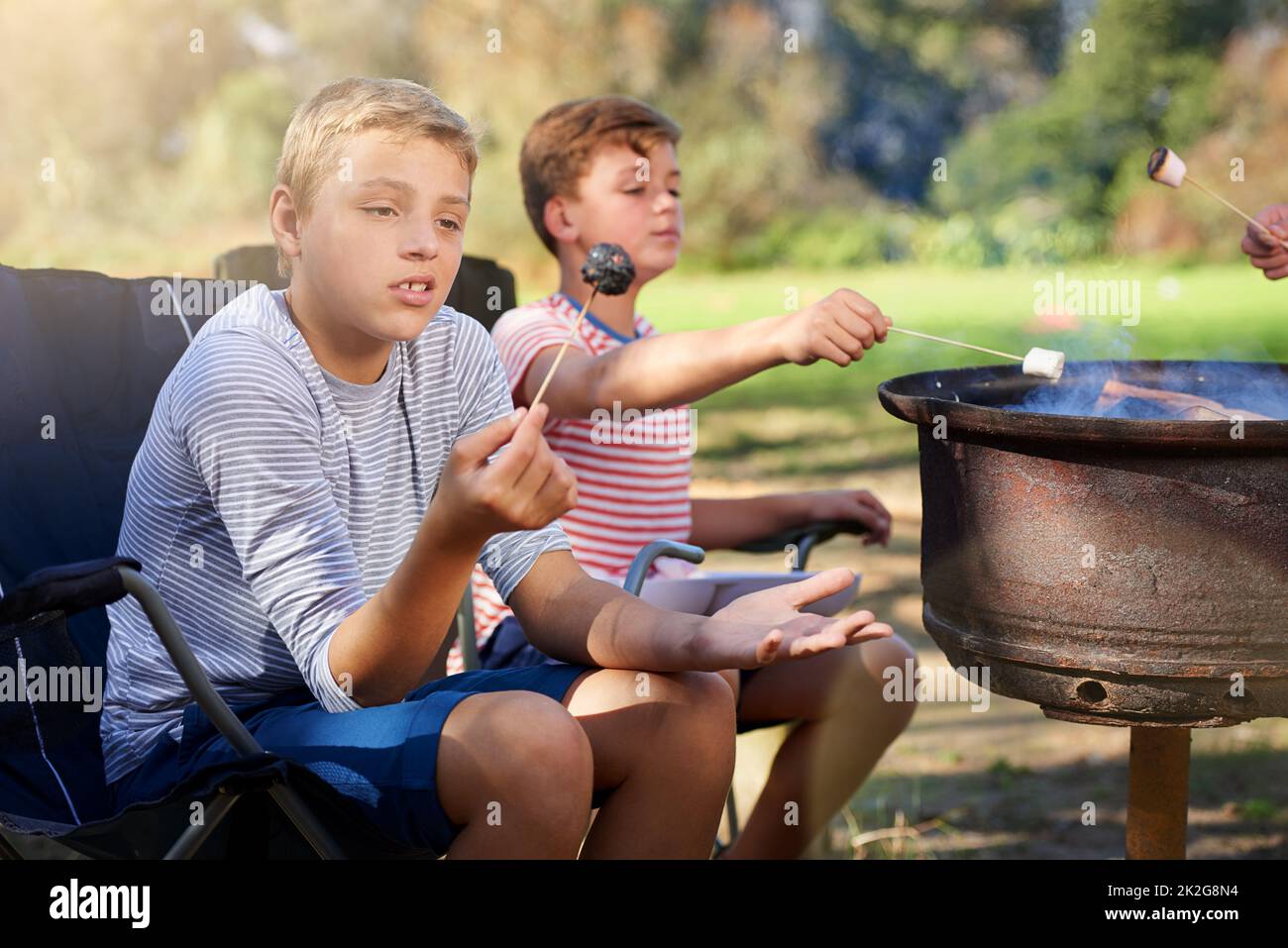 Errore.... Un ragazzo giovane che si guarda deluso dopo aver bruciato la sua marshmallow sul fuoco. Foto Stock