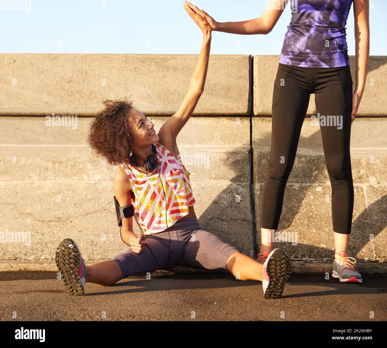 Entrambi abbiamo fatto stupendo. Shot di una jogger femminile seduta sulla strada e high-fiving suo partner in piedi. Foto Stock